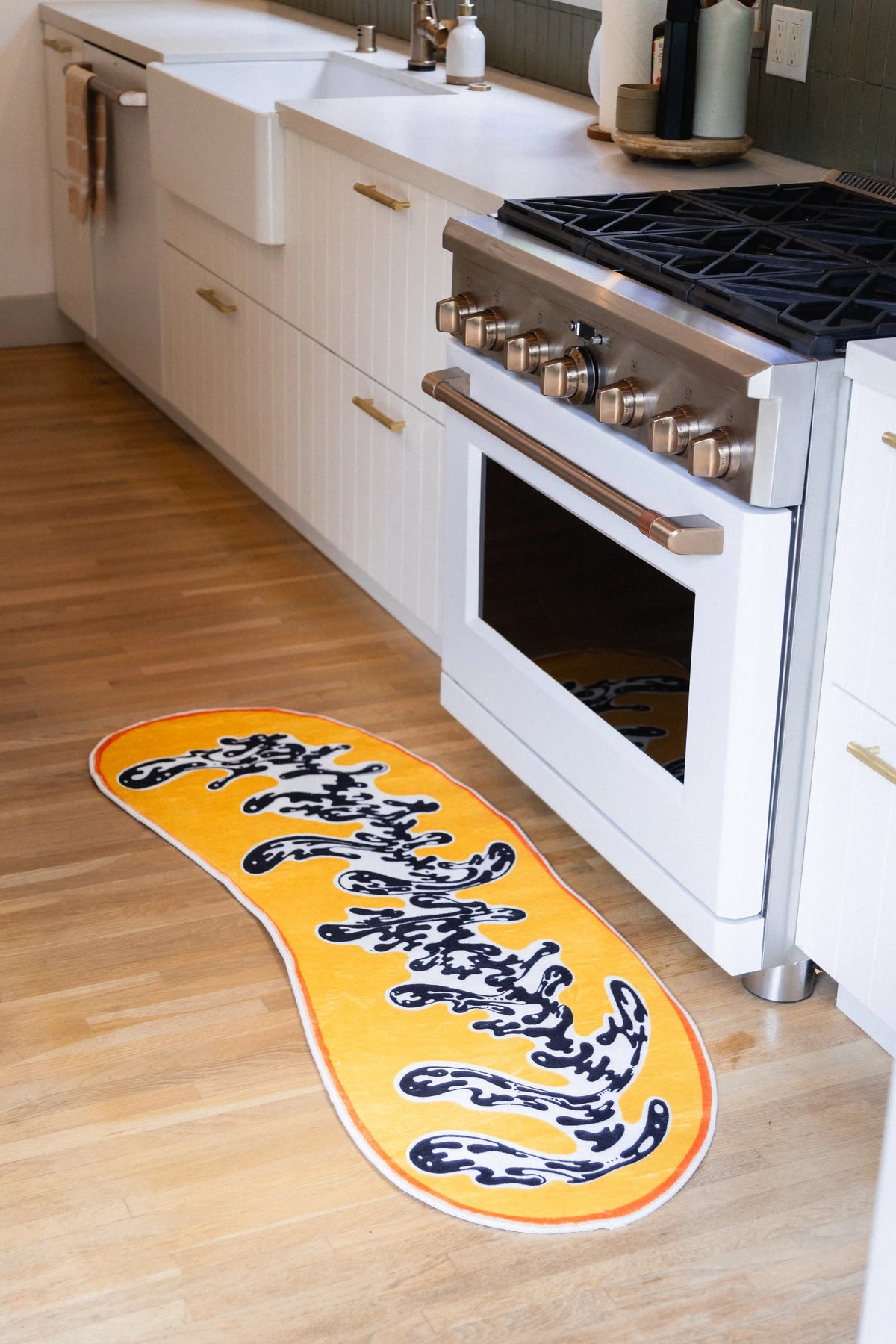 A narrow yellow runner brings its irregular outline and black-and-white motif to the space beside a white kitchen range.