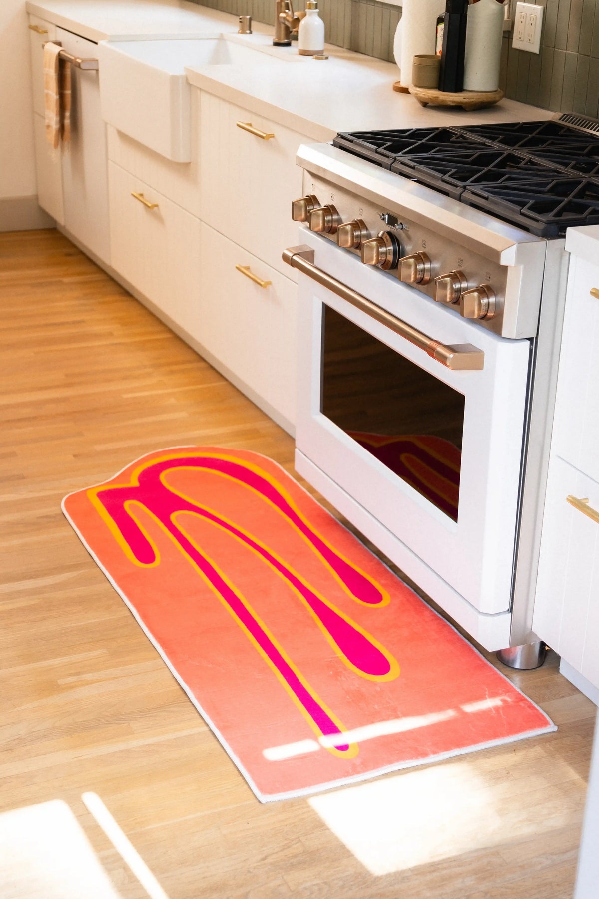 2' × 5' coral orange runner rug positioned in front of a white kitchen range on light wood flooring.