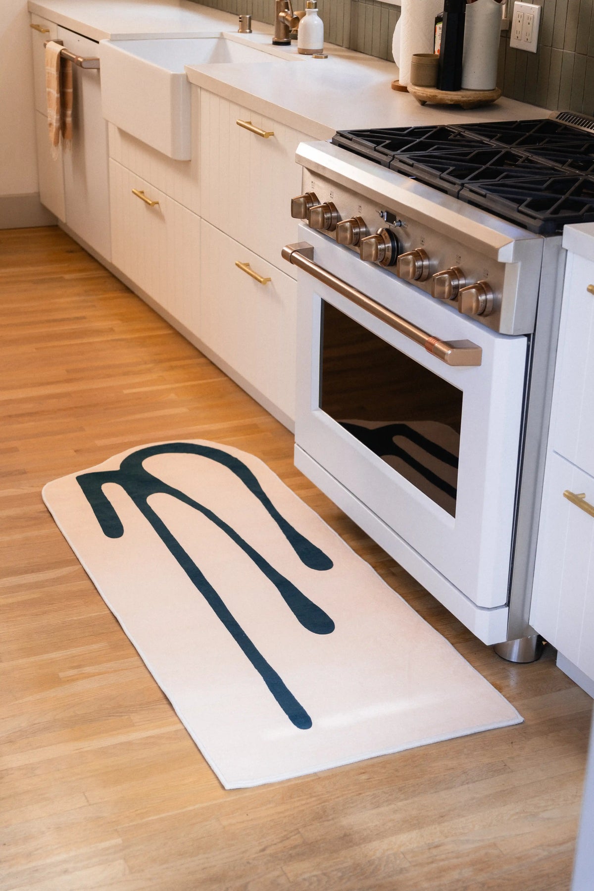 2' × 5' beige runner with a green drip pattern beside a white kitchen range on wood flooring.