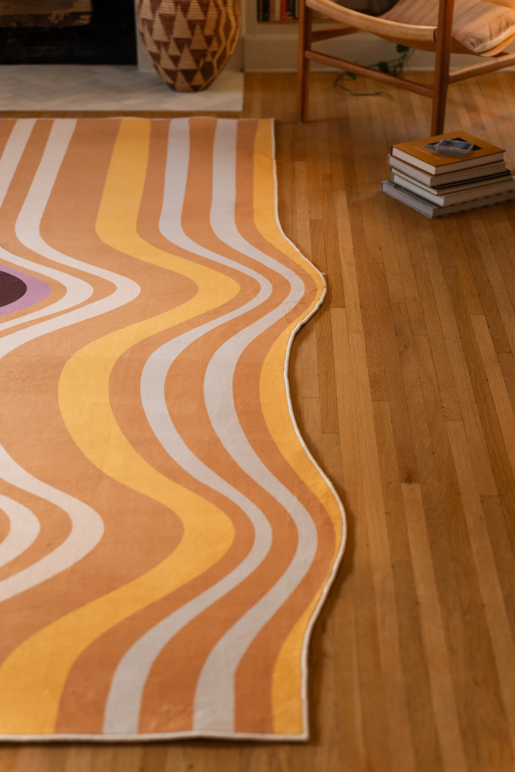 Long crop of the striped rug on a light wood floor, with stacked books at the edge and flowing warm color bands