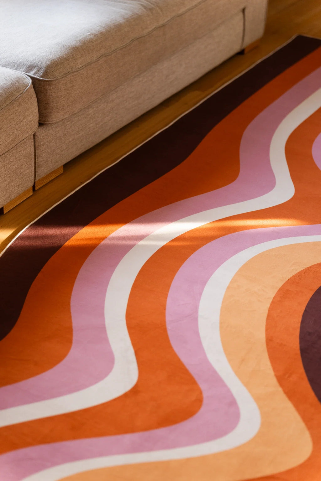 Partial close up of the Brown Abstract Striped Rocks rug beside a sofa, highlighting layered contour lines