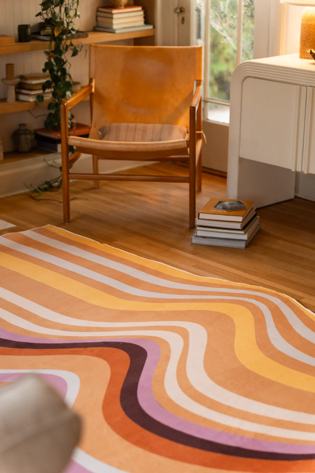 Wavy striped rug near a wood chair and white cabinet, showing soft tan, peach, cream, and plum curves