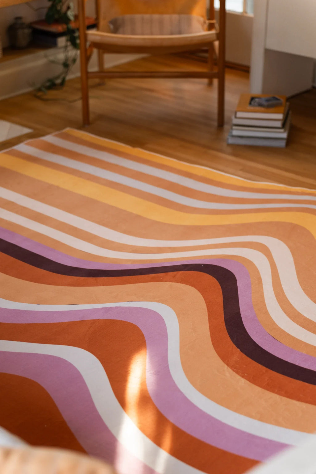 Rug detail beneath a chair, with sinuous brown and mauve bands sweeping across the light wood floor
