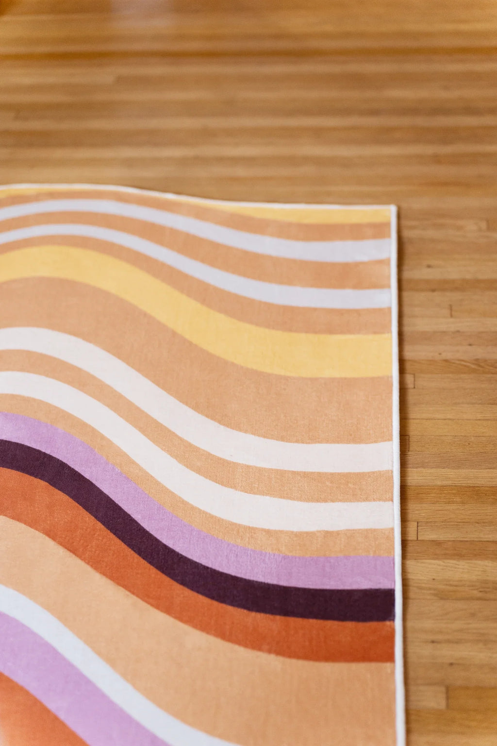 Corner close up of the abstract striped rug with cream, beige, lilac, and deep brown contours