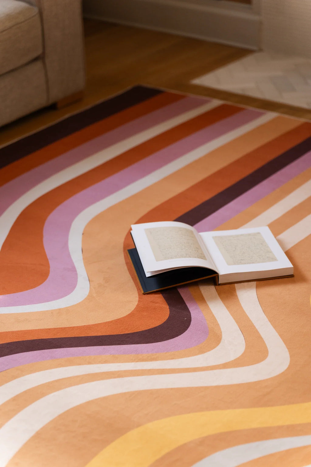 Open book resting on the striped rocks rug, with layered geological lines in tan, blush, cream, and brown