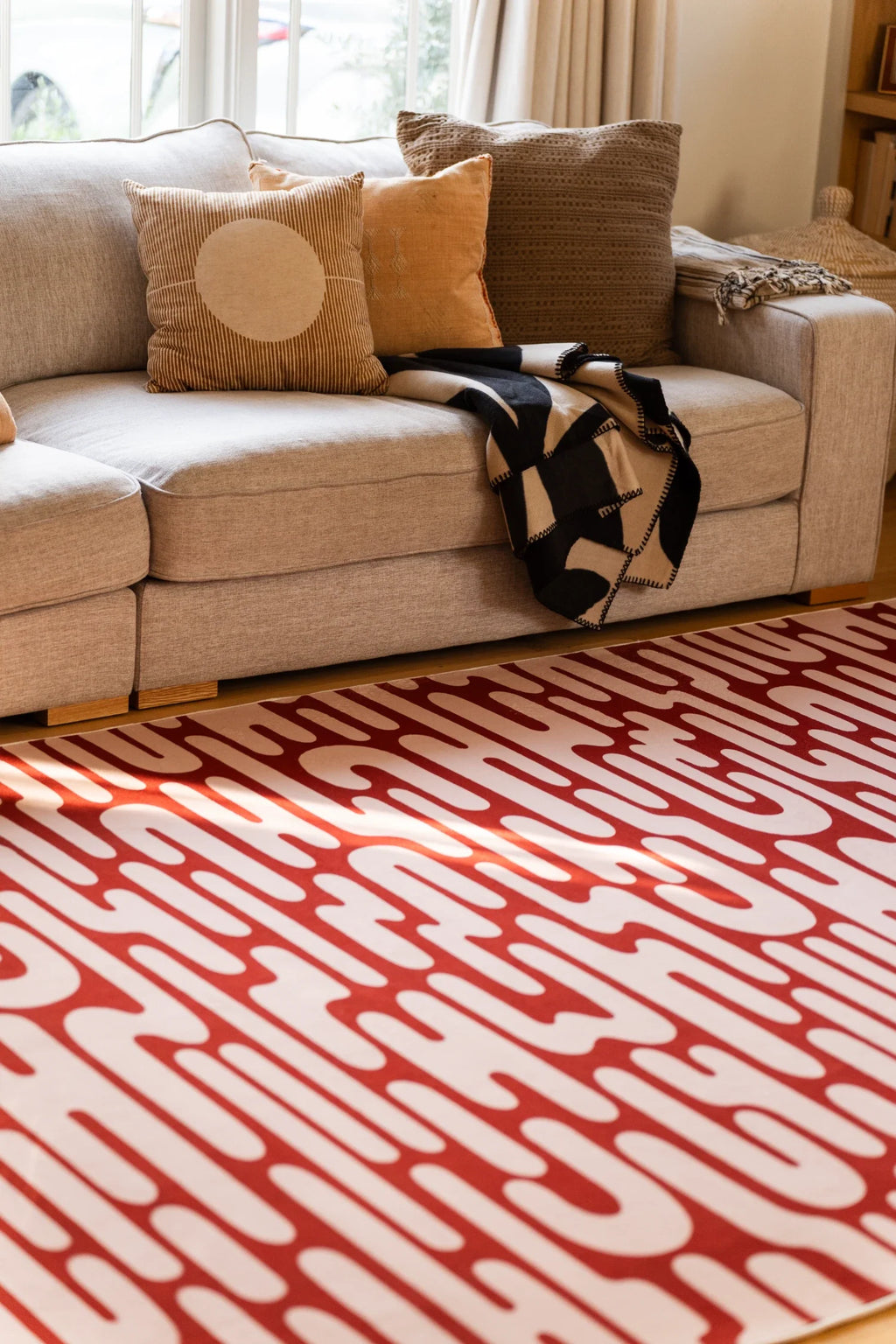 Brown Abstract Wavy Area Rug beneath a cream sofa in a warm living room with layered neutral pillows