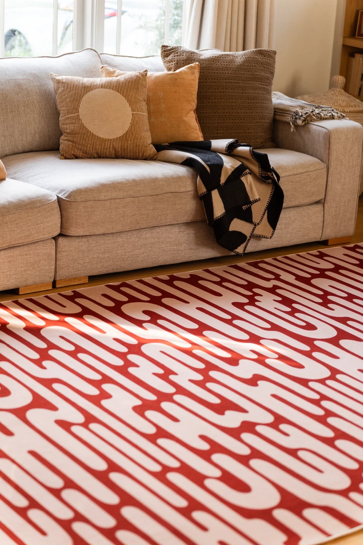 Brown Abstract Wavy Area Rug beneath a cream sofa in a warm living room with layered neutral pillows