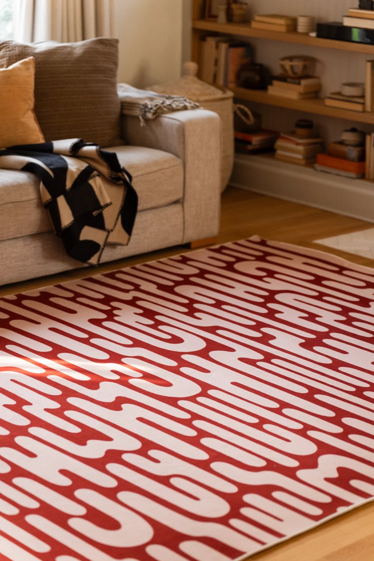 Brown Abstract Wavy Area Rug in front of a cream sofa in a relaxed modern living room with open shelving