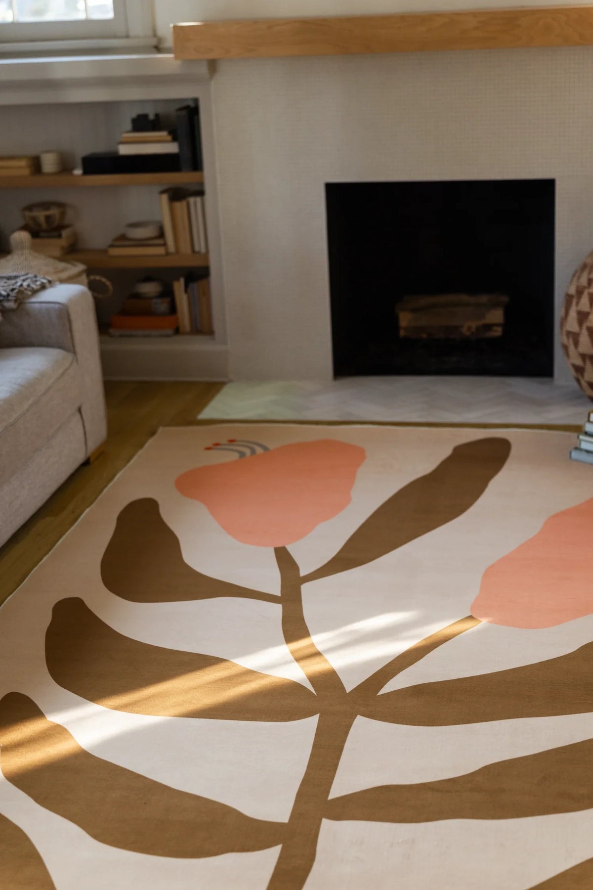 Close crop near the fireplace with the floral rug's brown stem and leaf pattern stretching across a beige ground