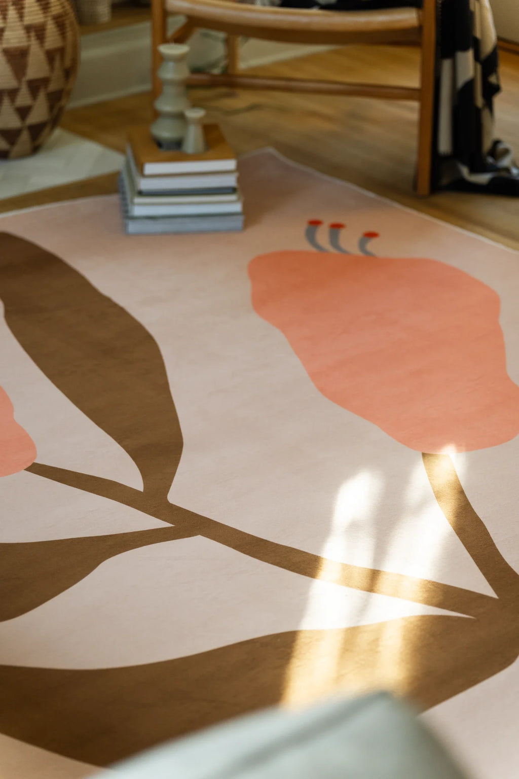Close view with sunlight across the floral rug, highlighting a peach bud and broad brown leaf shapes