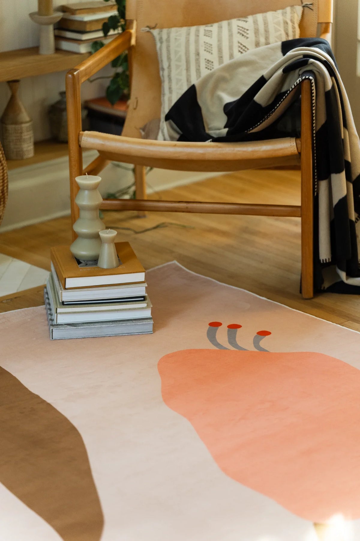 Vintage flower rug beside a wood chair and books, showing a peach bloom and branching brown stem on a beige background