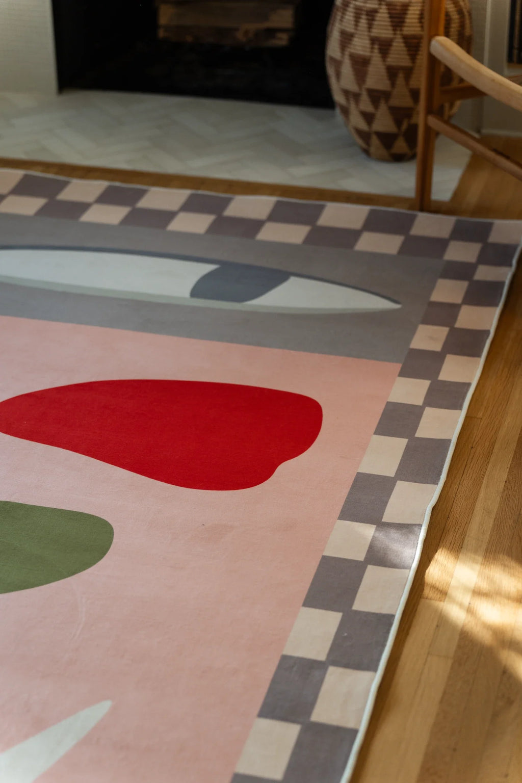 Close up of the blush pink area rug near the fireplace, showing a red petal, olive stem, and checker border