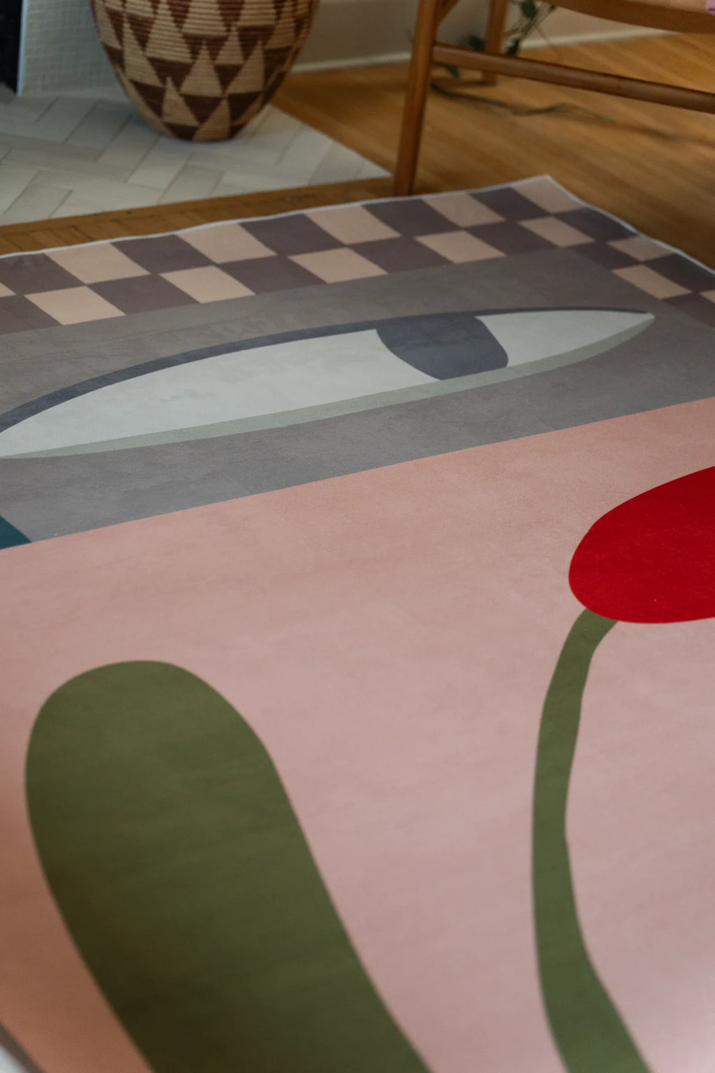 Partial rug detail with an olive green stem and red flower bud on a blush ground beside a woven basket