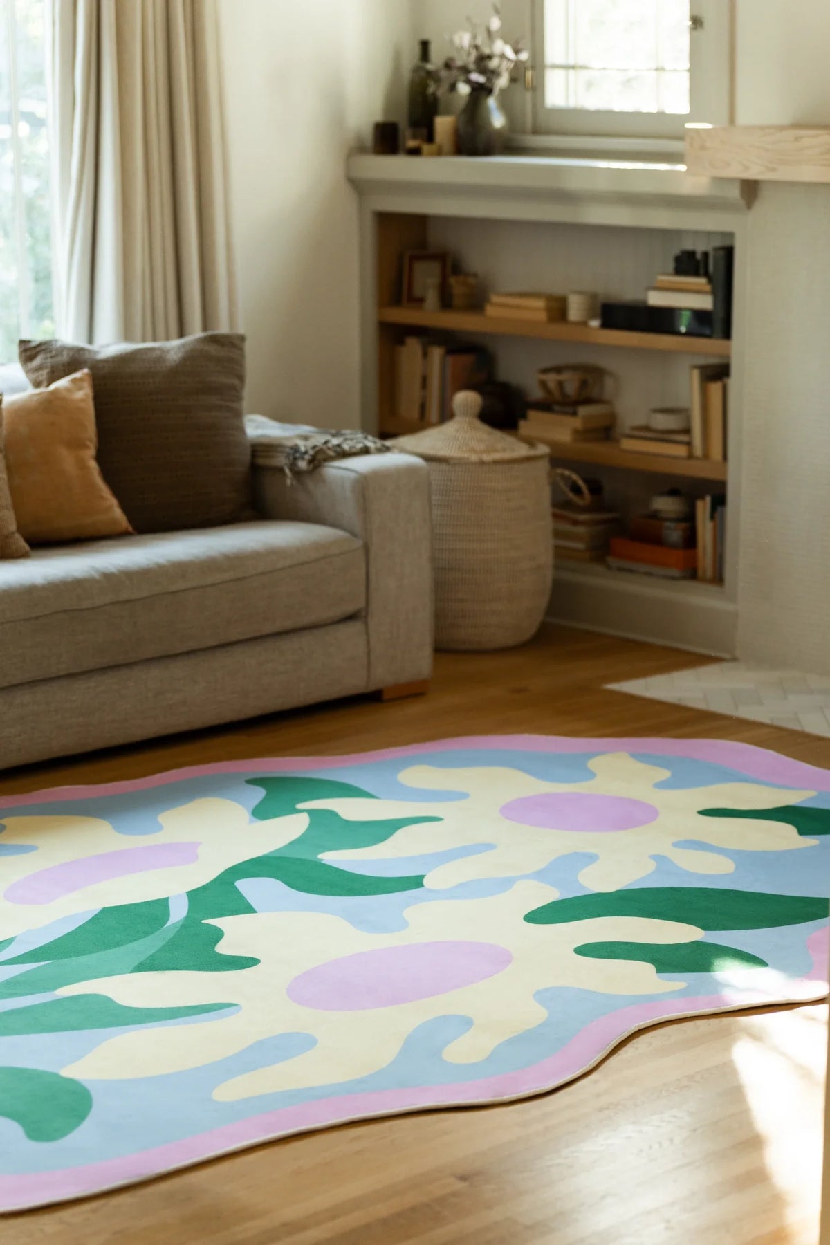 Colorful abstract floral rug tucked under a beige sofa, with lilac flowers and dark green leaf shapes across the surface