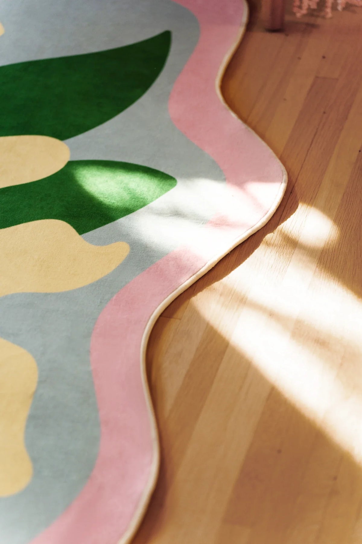Close up of the irregular shaped floral rug showing the wavy pink border and pastel flower forms in sunlight