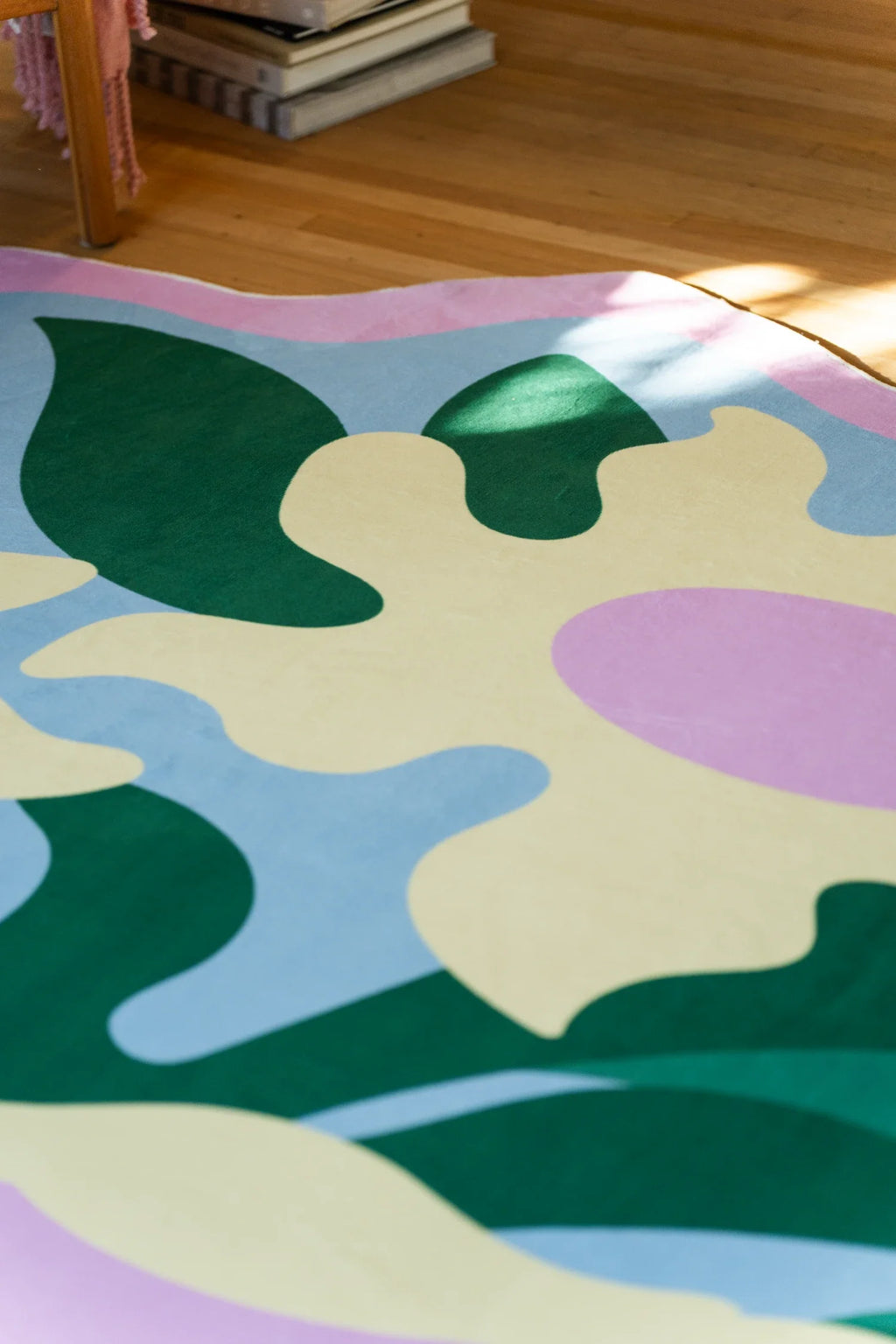 Corner detail of the abstract flower rug with curved green leaves, pale yellow petals, and a softly scalloped pink edge