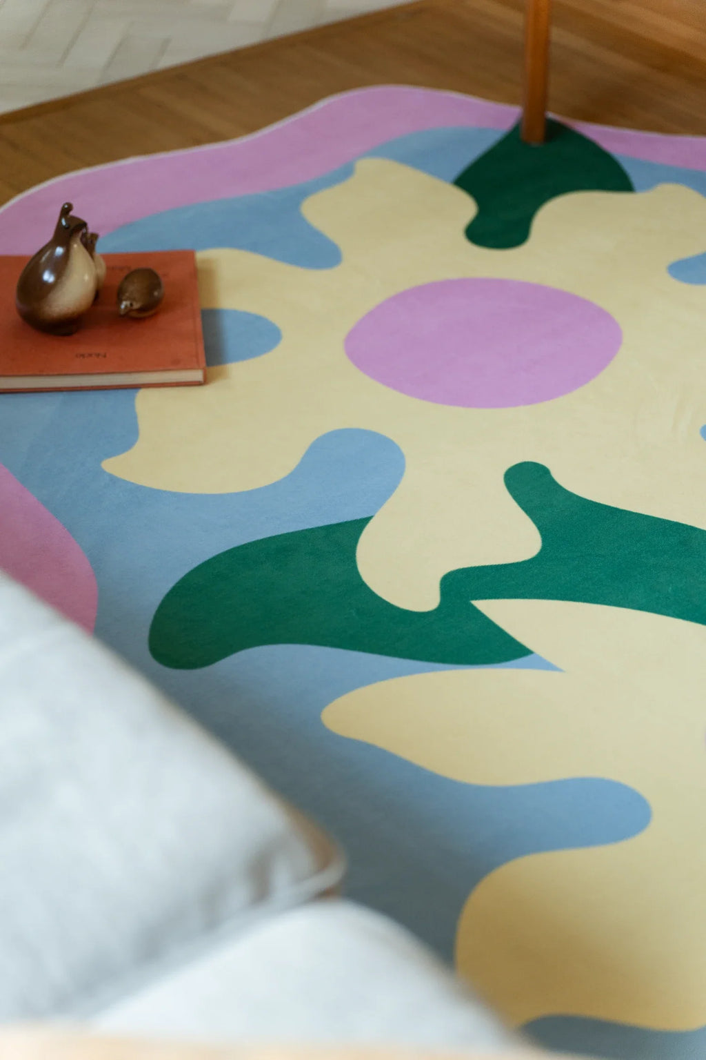 Close up of the colorful floral rug beneath a chair leg, showing lilac petals, pale yellow shapes, and flowing green forms