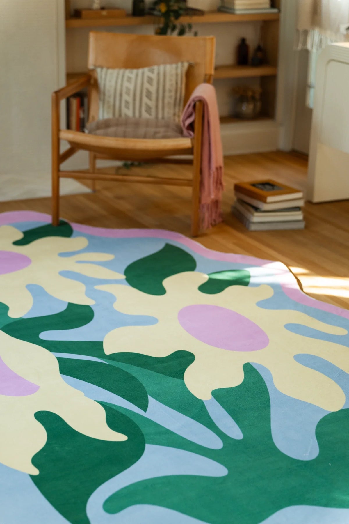 Partial view of the irregular floral rug near a wood chair, showing broad green leaves and rounded lavender flower forms