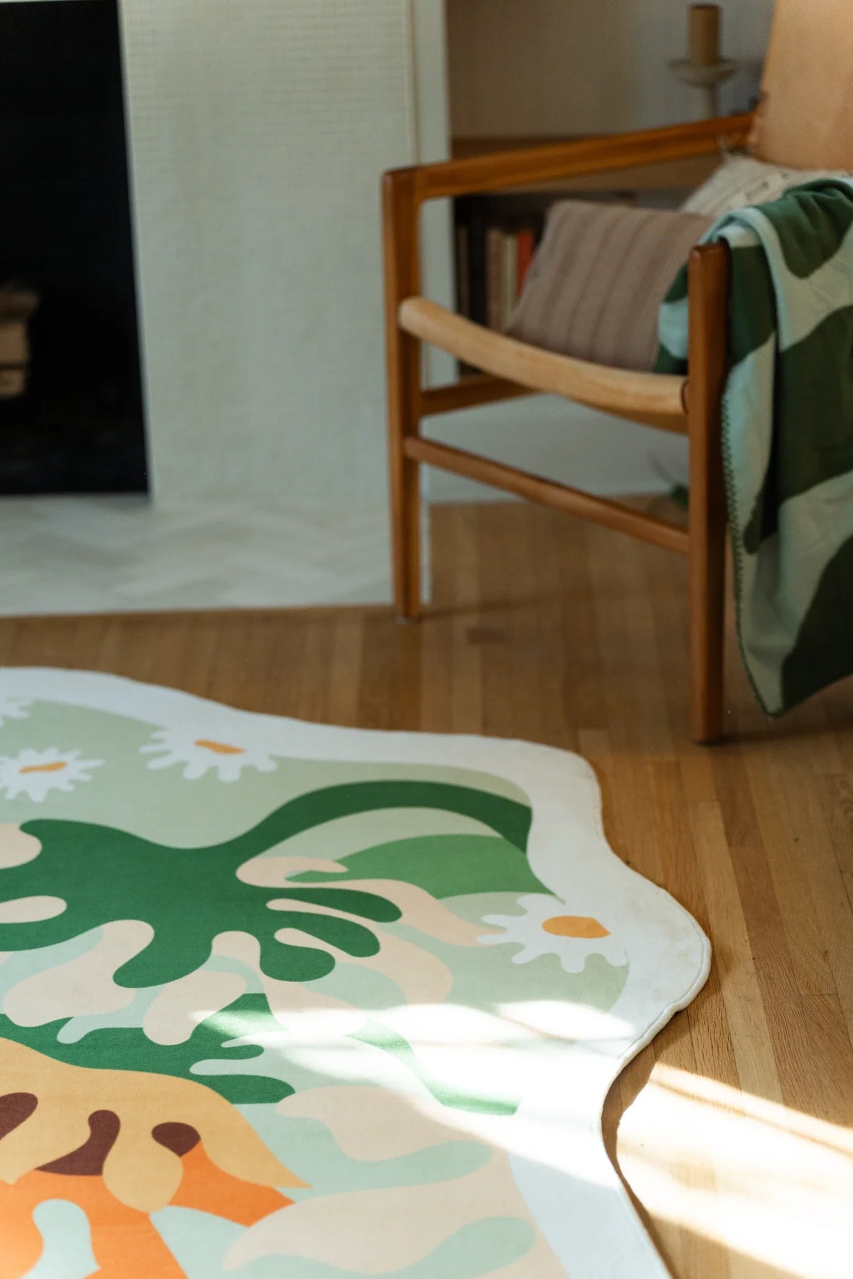 Close up of the soft green sunflower rug beside a green pillow and cream rotary phone, showing orange blooms and white flowers