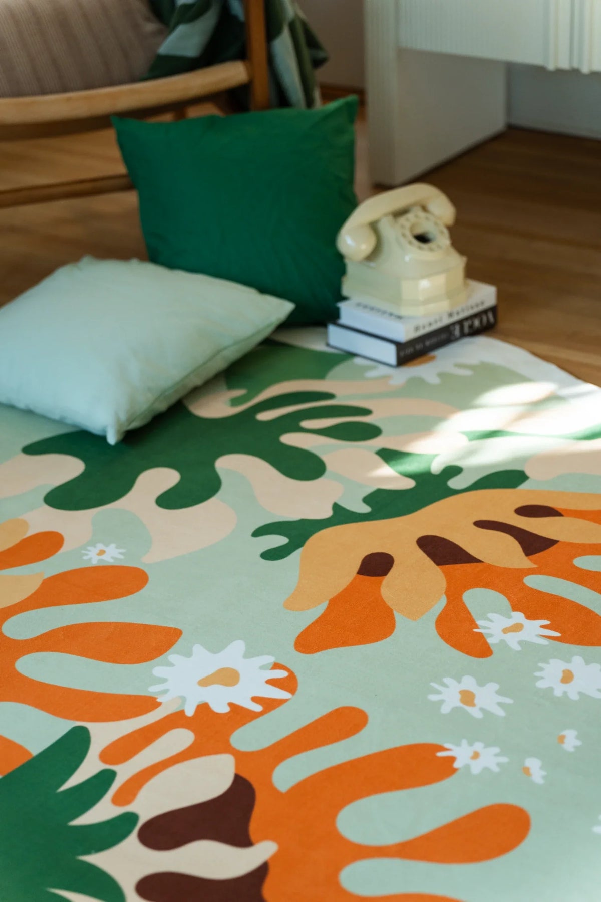 Soft green floral rug beside a neutral sofa and woven basket, with scattered white daisies and orange botanical forms