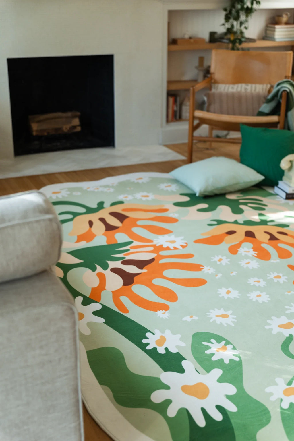 Partial view of the floral rug under a sofa edge, with orange sunflower petals and broad green leaves on a soft green field