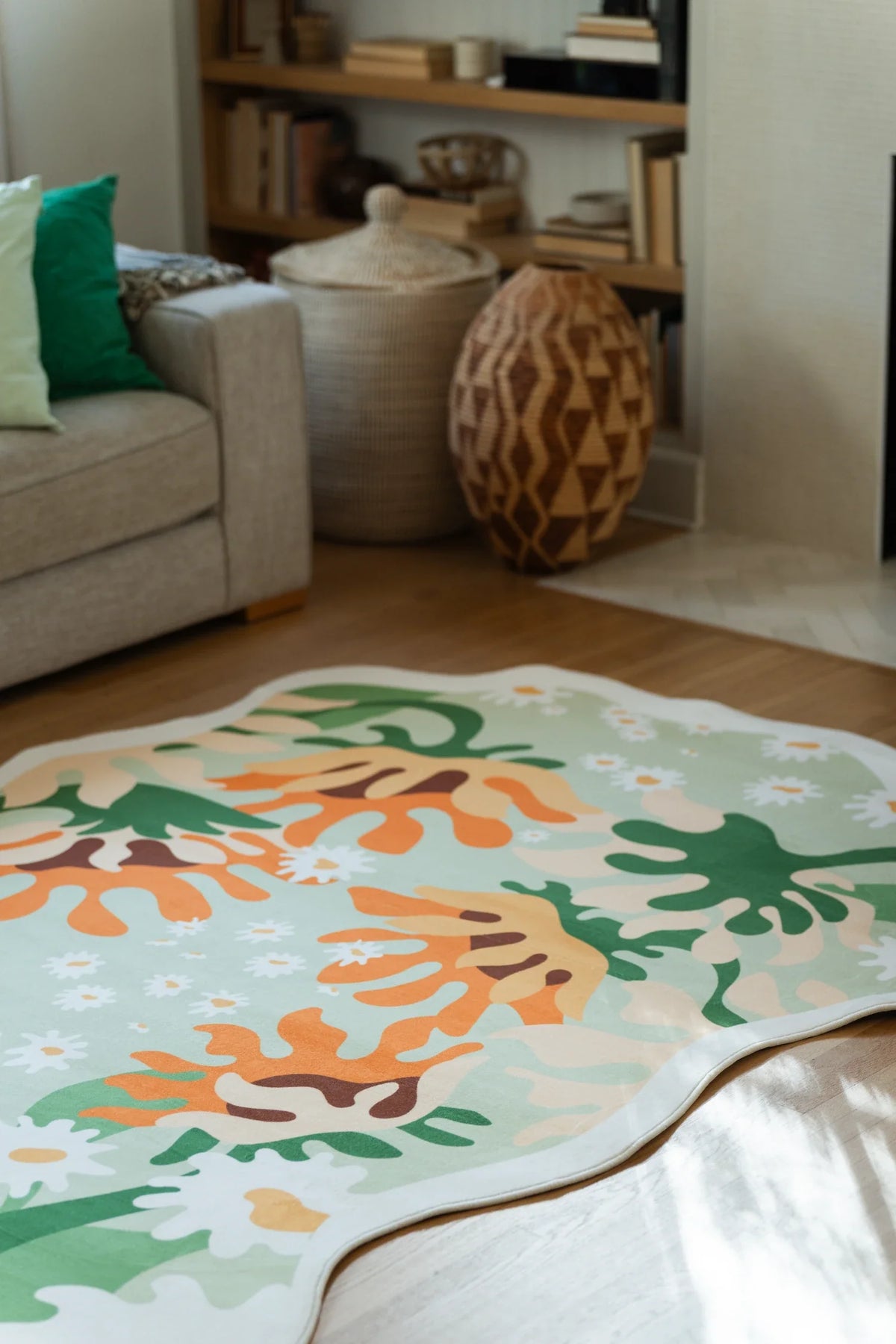 Corner crop of the irregular shaped rug near the fireplace and chair, showing green leaf silhouettes and a cream edge