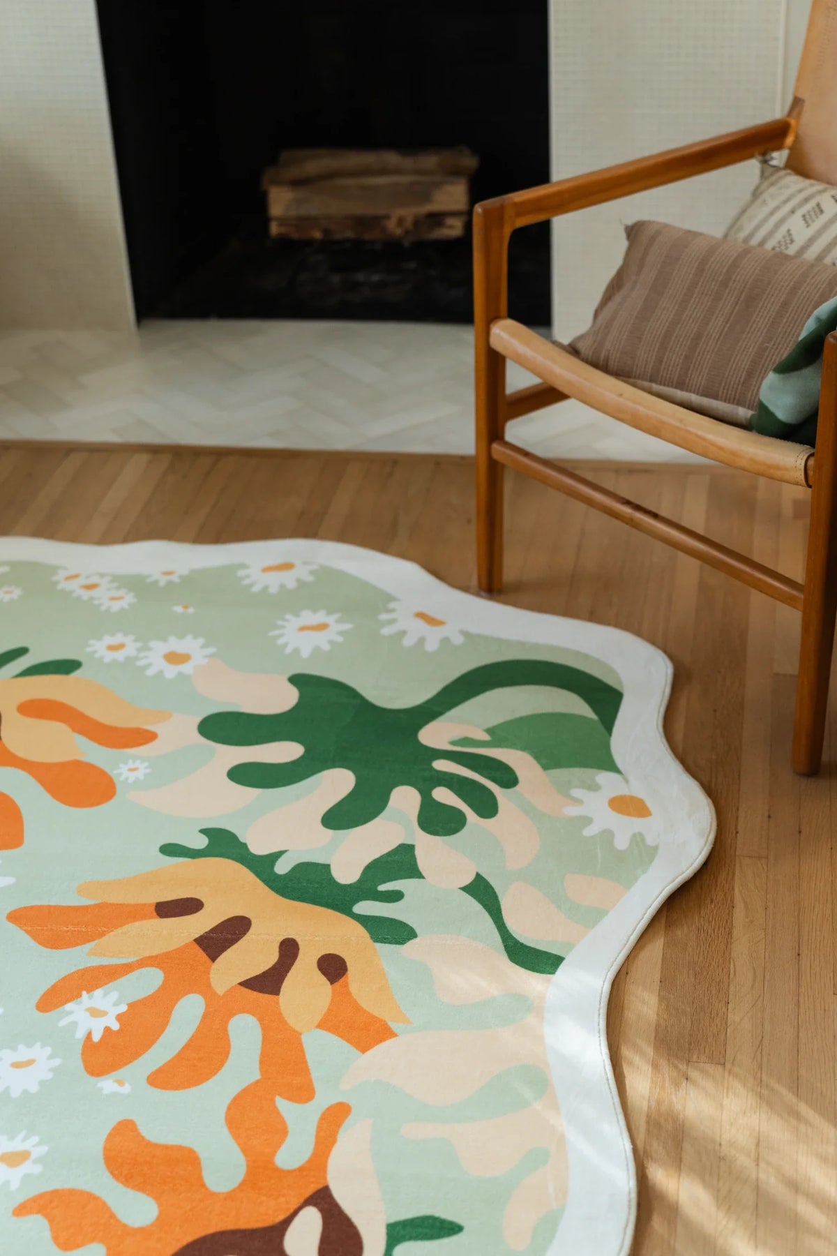 Sunflower floral area rug on a light wood floor beneath a wood chair, with orange petals, green leaves, and a wavy outline