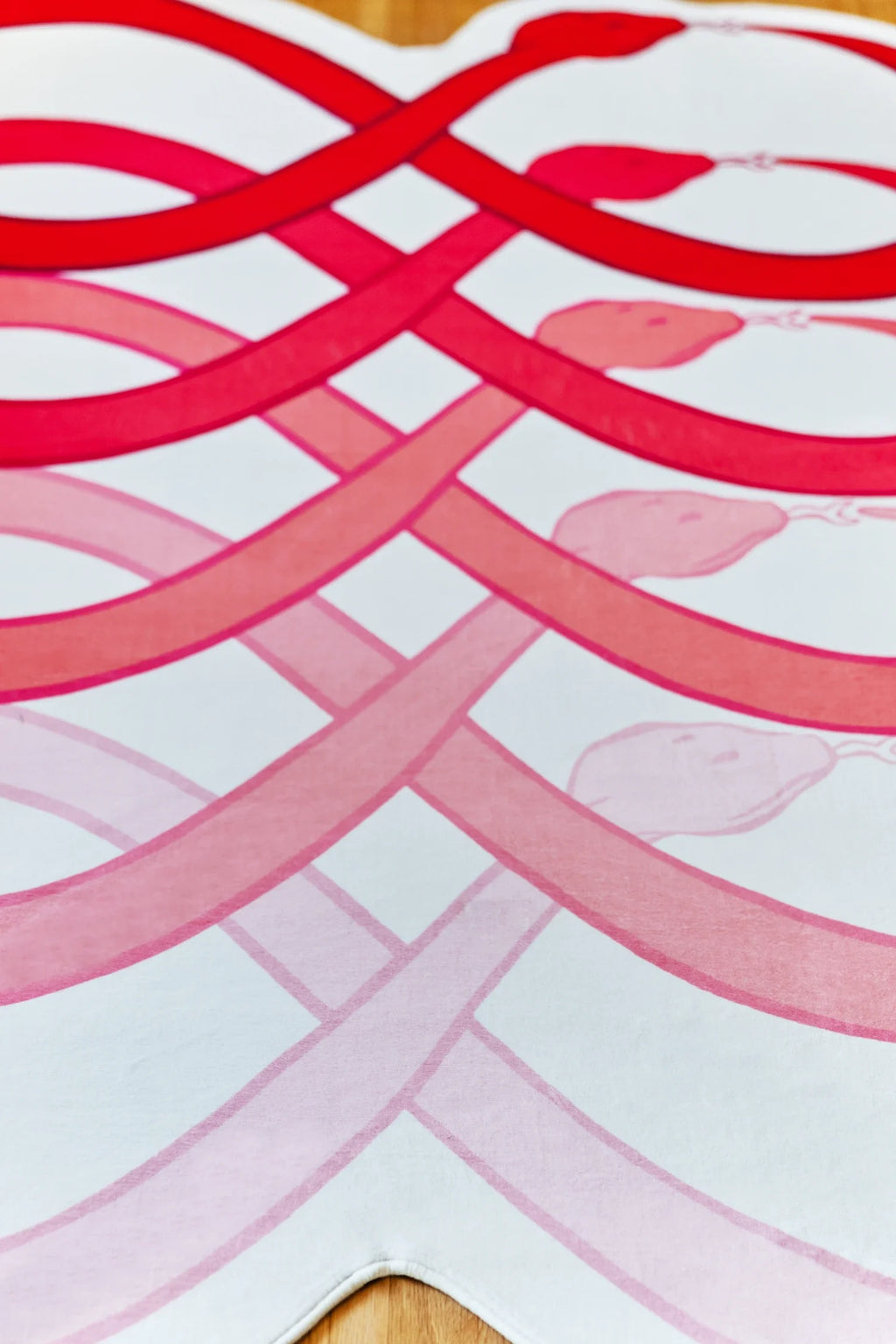 Red abstract loop rug on a light wood floor, with flowing curved stripes creating a layered snake pattern