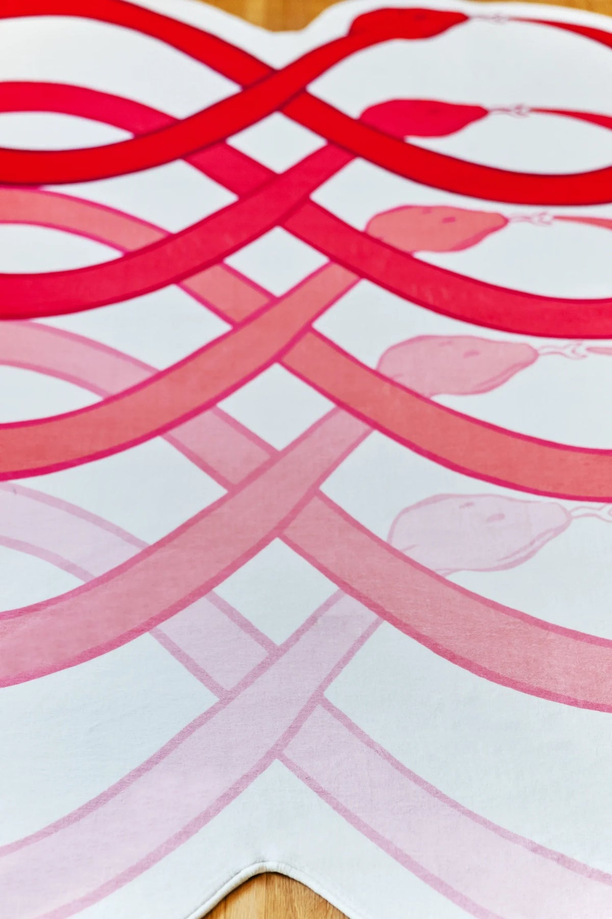 Red abstract loop rug on a light wood floor, with flowing curved stripes creating a layered snake pattern