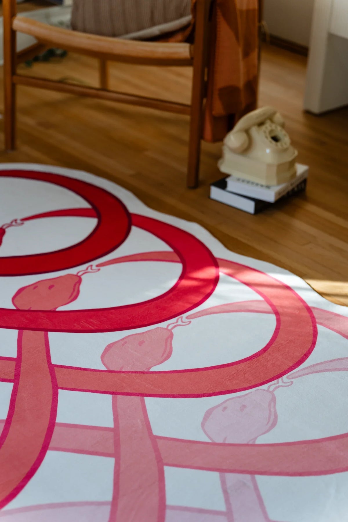 Red loop snake area rug beside a wood chair and small dog figurine in a bright living room corner