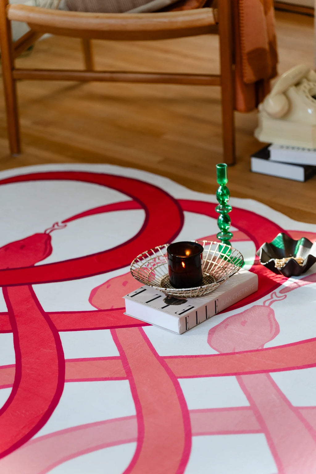 Abstract area rug with red looping bands beneath a tray with candles, styled on a light wood floor