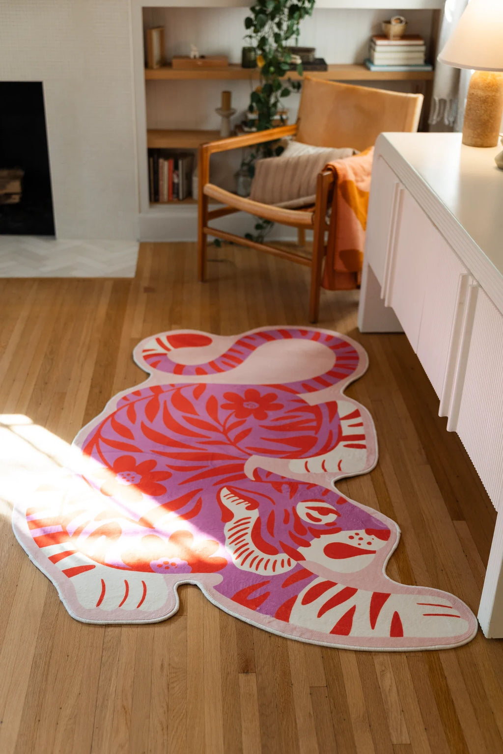 Irregular shaped tiger rug laid between a wood chair and fireplace, with the crouching silhouette fully visible
