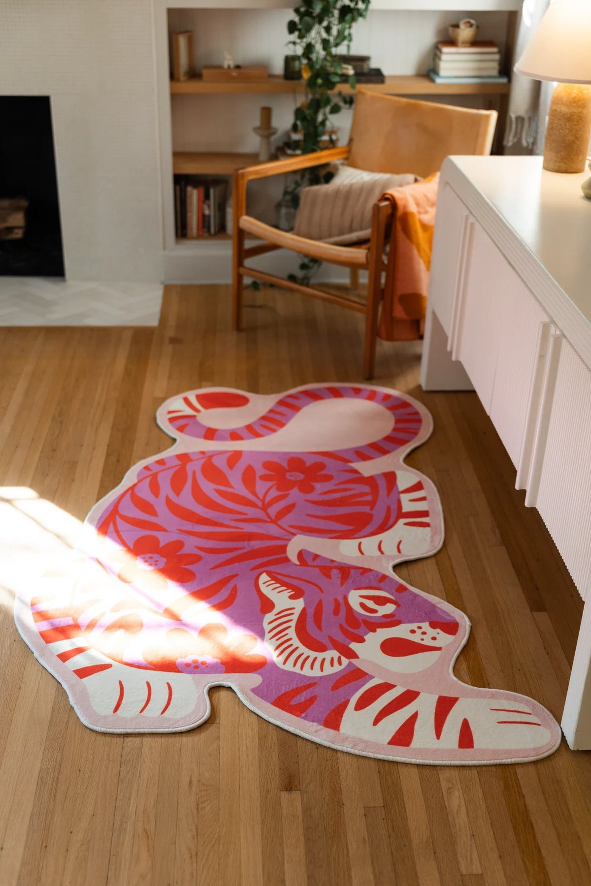 Irregular shaped tiger rug laid between a wood chair and fireplace, with the crouching silhouette fully visible