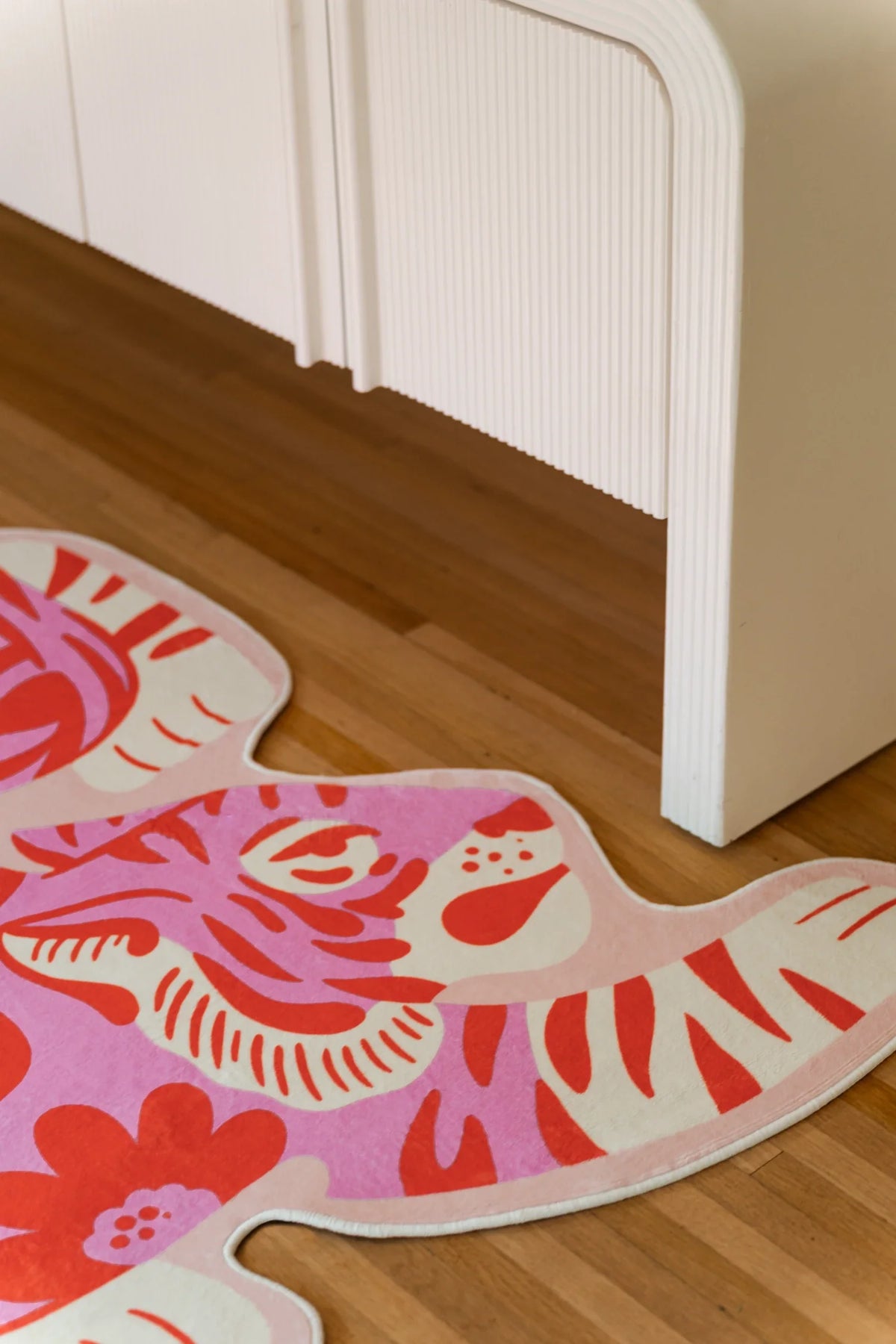 Partial crop near white cabinetry, showing the tiger rug's curved flank, white edge, and coral stripe bands