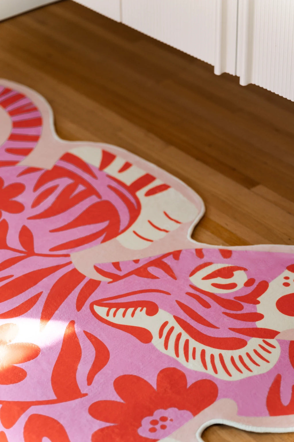 Corner crop of the irregular shaped rug near white cabinetry, focused on the tiger head and striped cheek detail