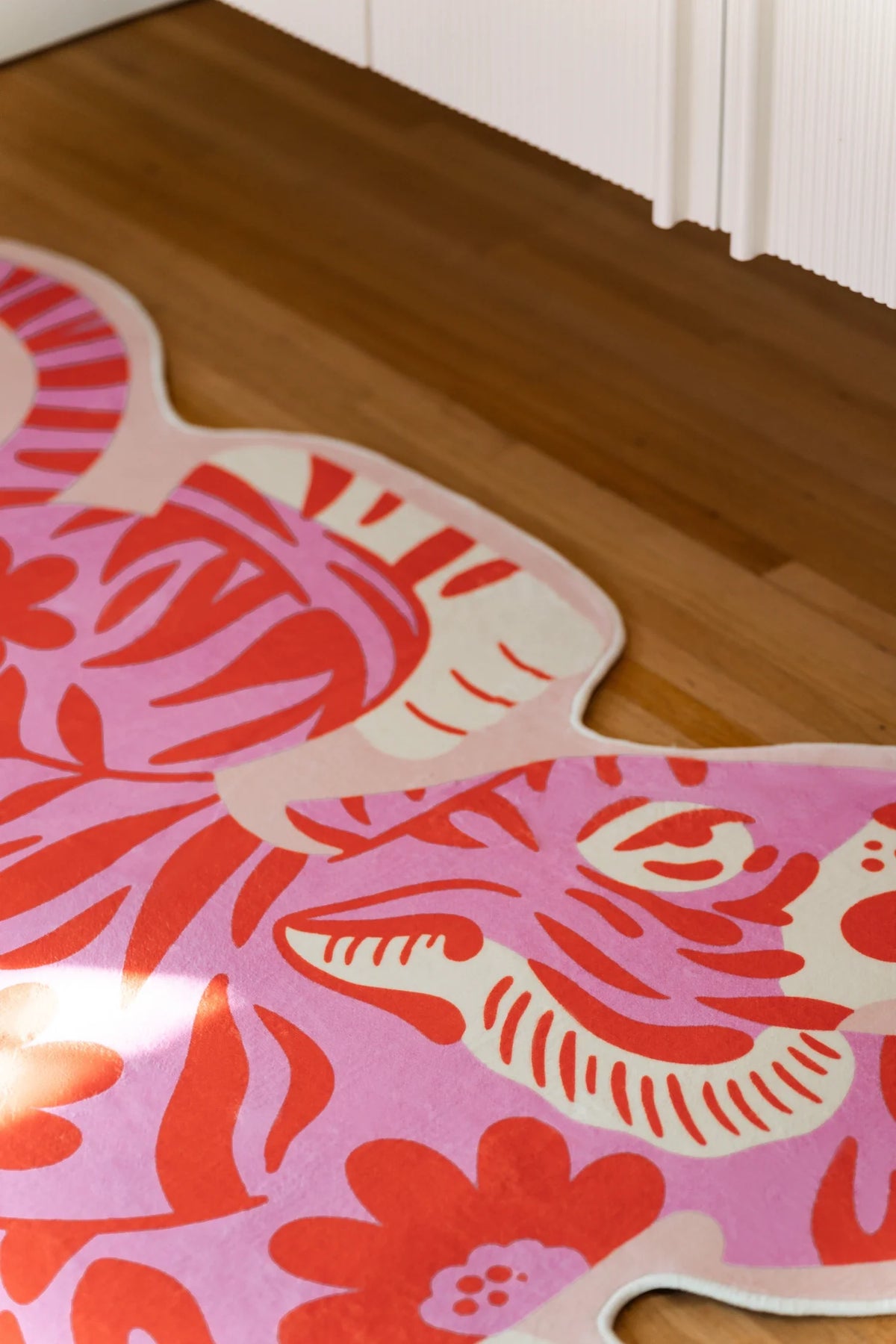 Corner crop of the irregular shaped rug near white cabinetry, focused on the tiger head and striped cheek detail
