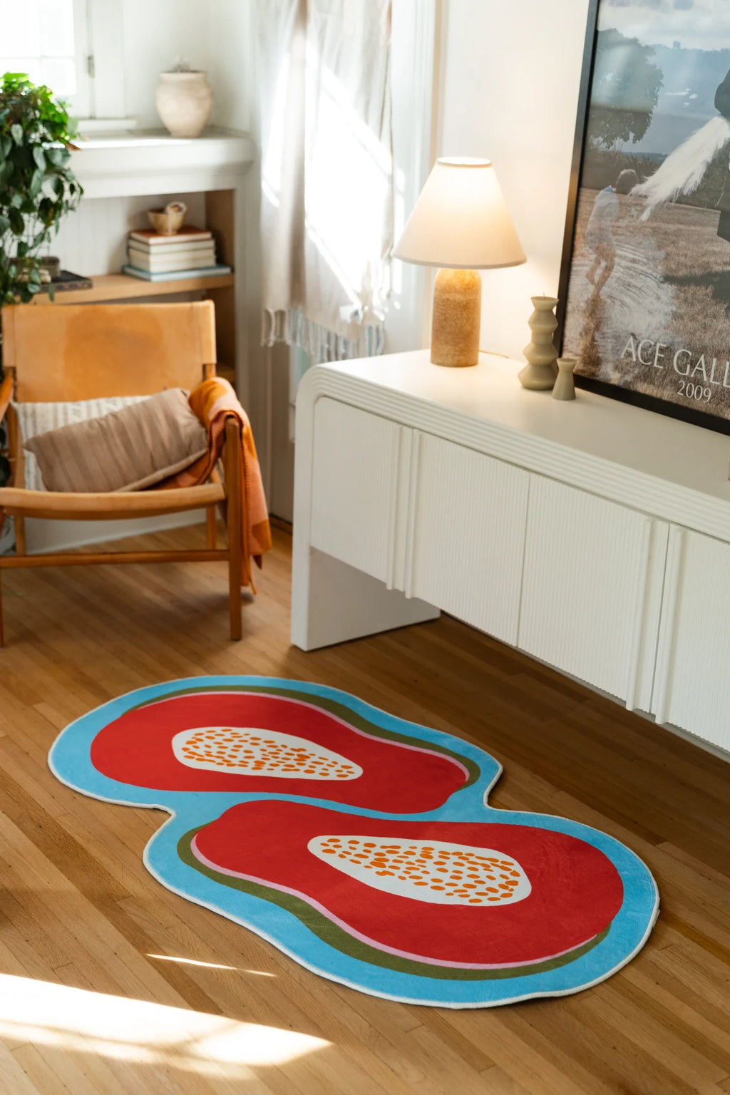 Orange papaya rug beside a wood chair, floor lamp, and white media cabinet on a sunlit wood floor