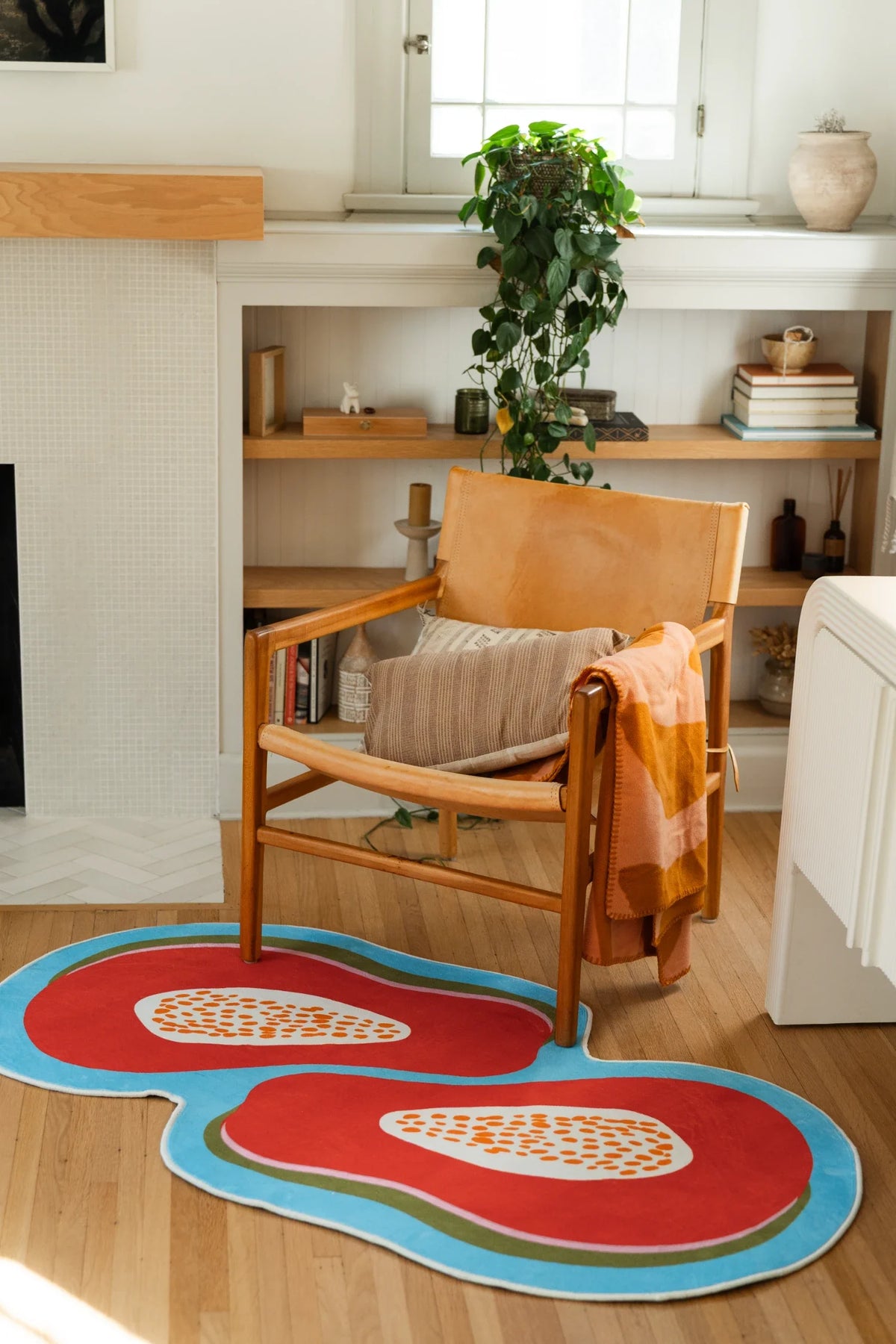 Papaya fruit rug in a bright reading corner with a wood lounge chair and white fireplace mantel