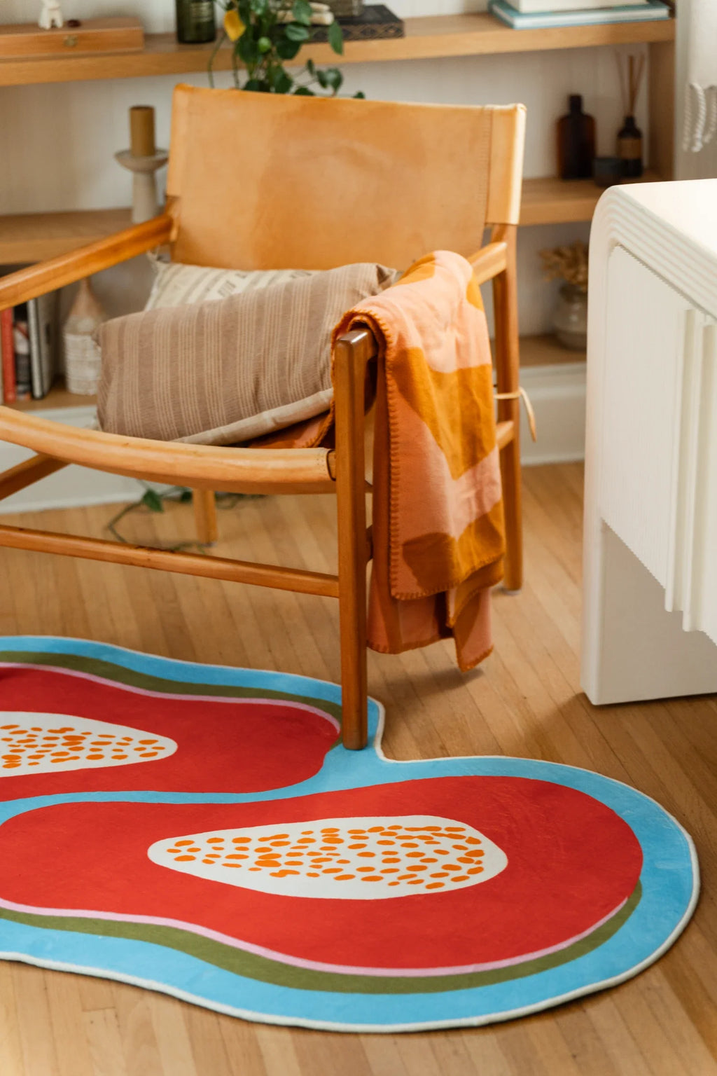 Papaya fruit rug near a wood chair and white cabinet, showing bright orange shapes with a sky blue border