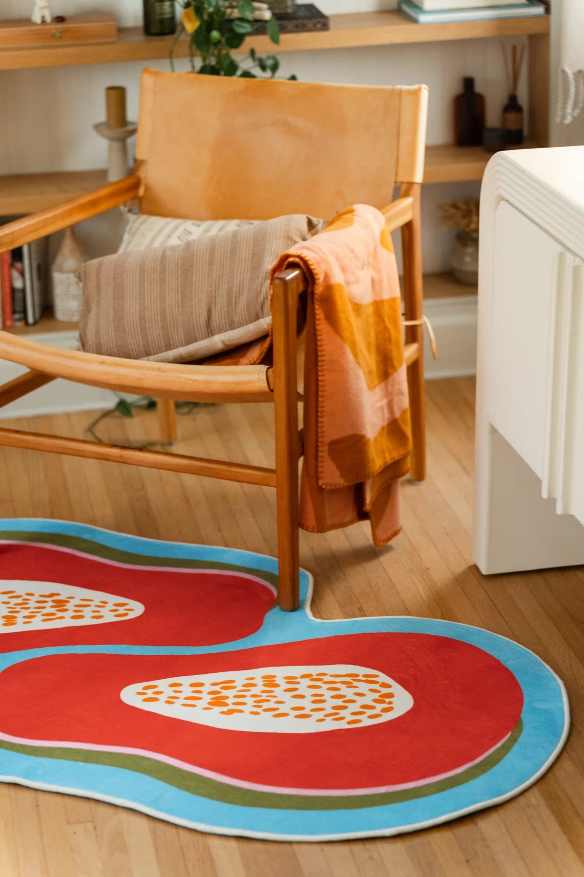 Papaya fruit rug near a wood chair and white cabinet, showing bright orange shapes with a sky blue border