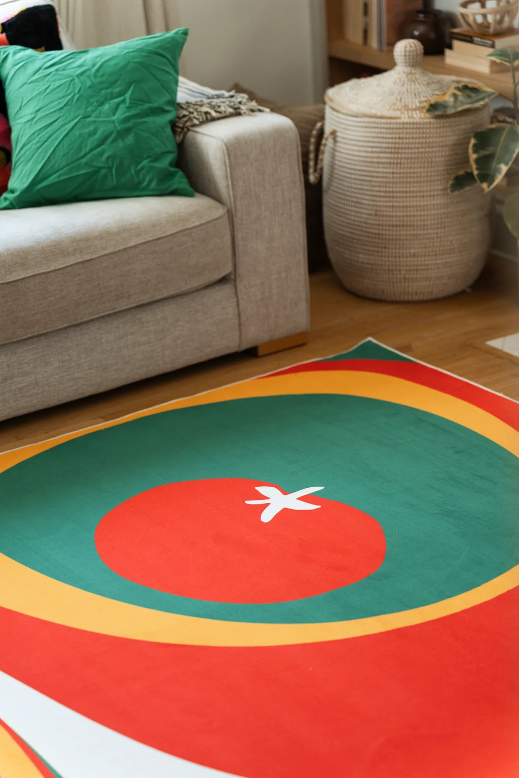 Olive and red Tomato Twist rug beside a beige sofa and woven basket, showing a red tomato circle