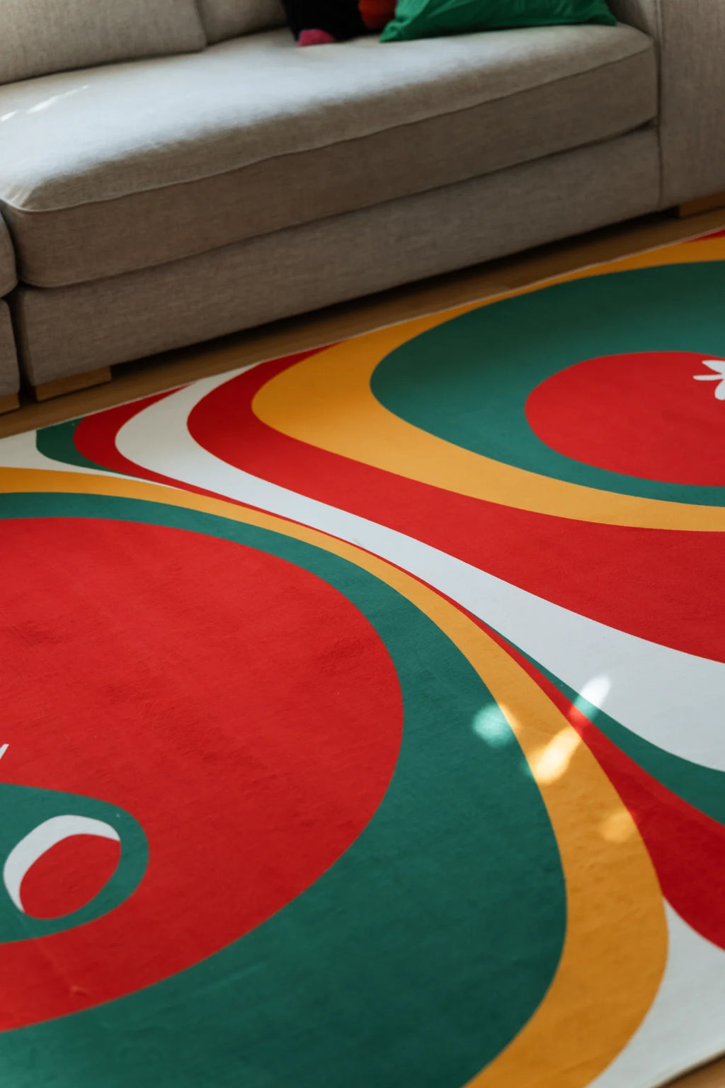 Olive and red abstract rug beneath a sofa edge, showing layered green, mustard, and white contour bands