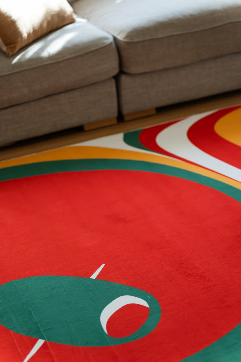 Close up of the olive and red rug beside a sofa, showing a large red circle and green tomato slice detail