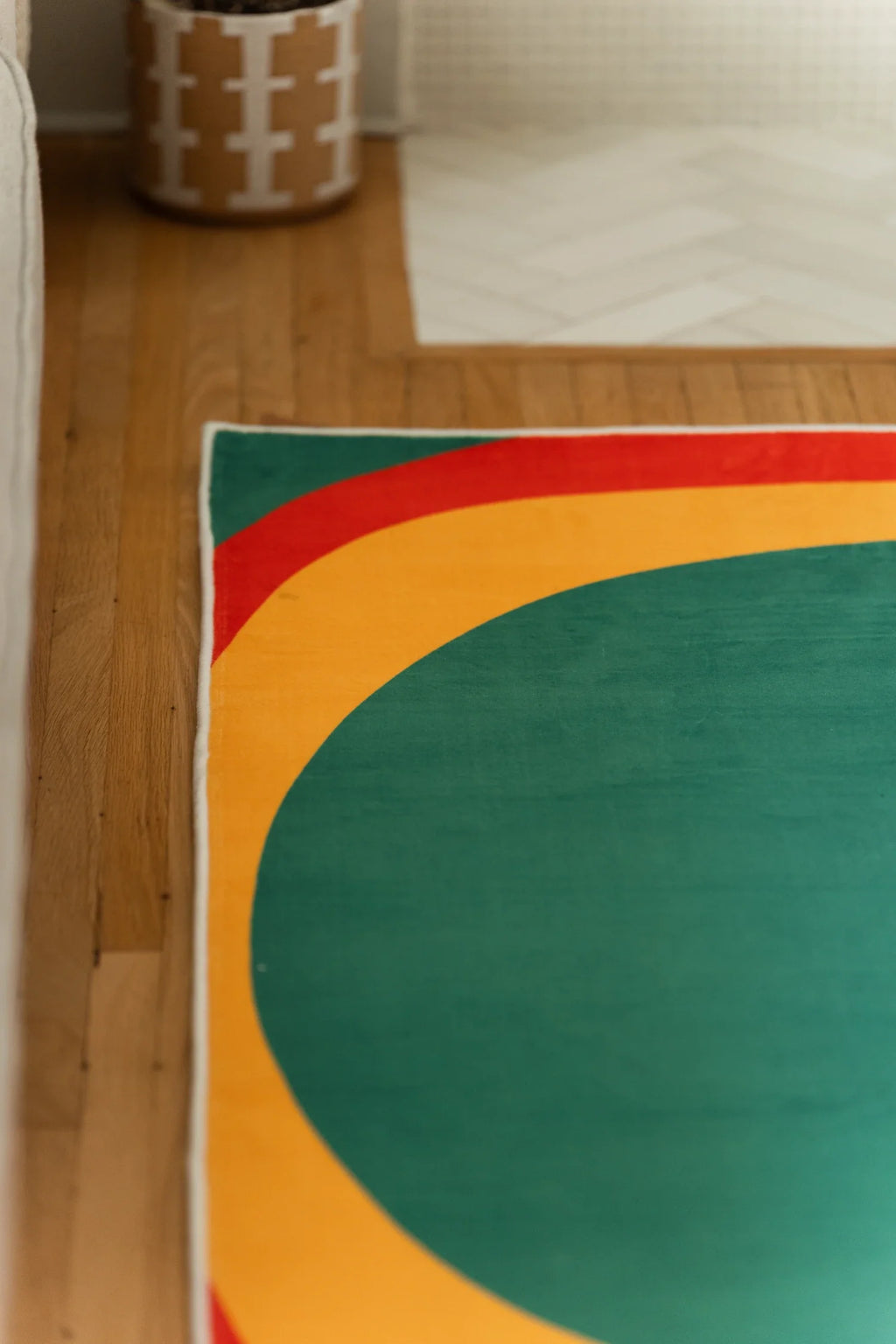 Close up of the olive and red rug edge on a wood floor, showing a large green circle and mustard border