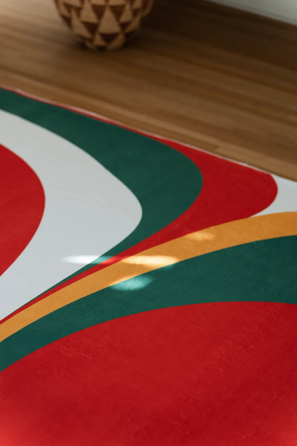 Partial view of the olive and red rug with sweeping white, mustard, and green curves around a red form