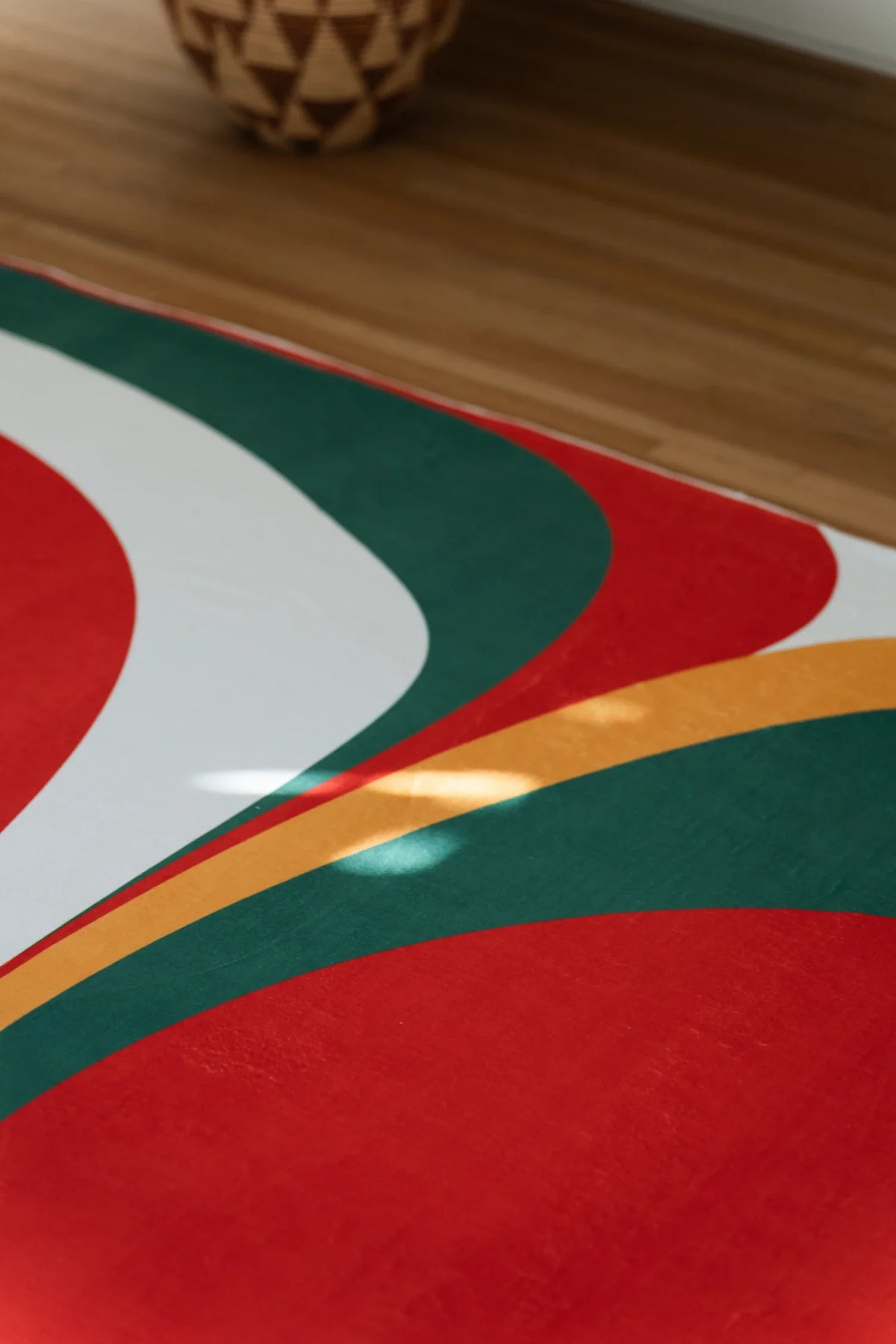 Partial view of the olive and red rug with sweeping white, mustard, and green curves around a red form