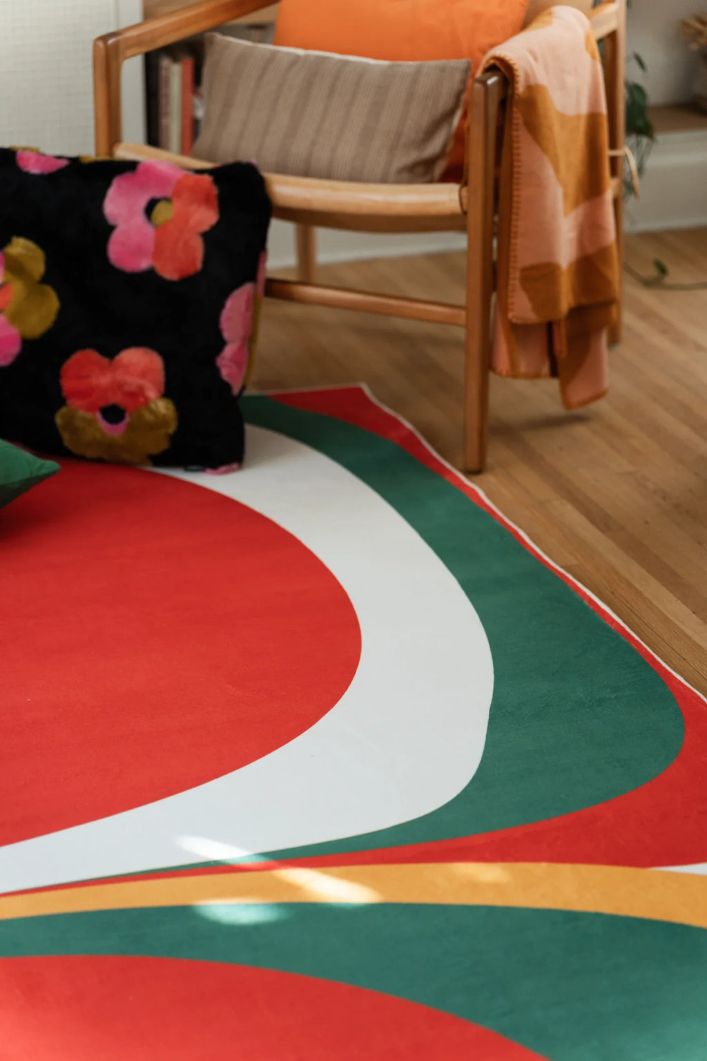 Close up of the olive and red rug beside a wood chair, showing curved white, green, and mustard bands