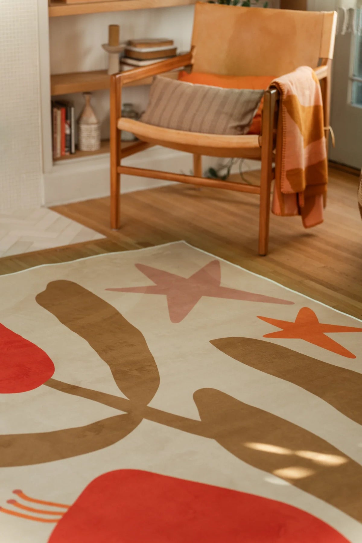 Red floral abstract rug near a wood chair and shelving, with rounded flower forms and sweeping tan stems