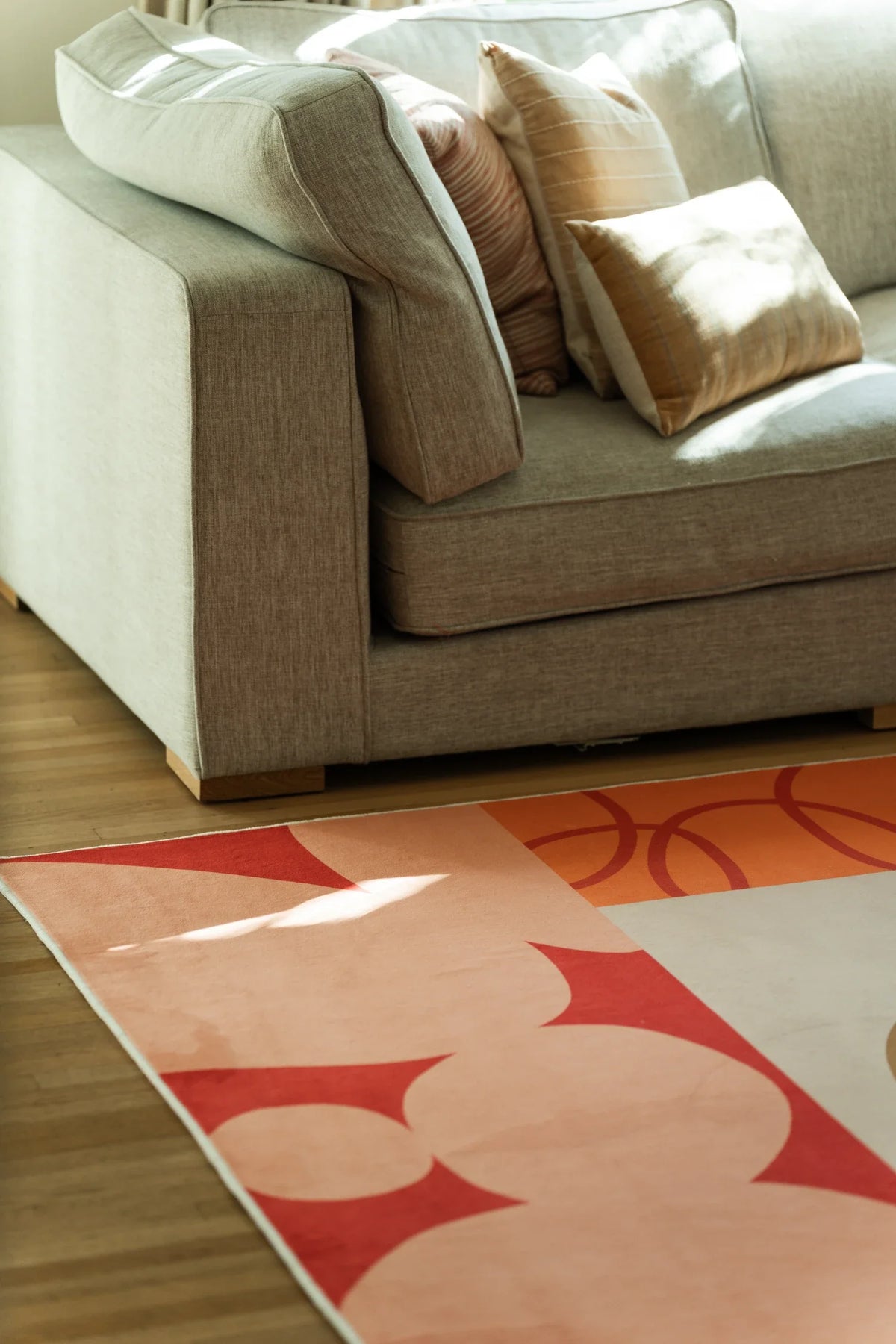Close crop under a sofa edge showing red floral blocks, a tan stem, and a pale pink corner panel