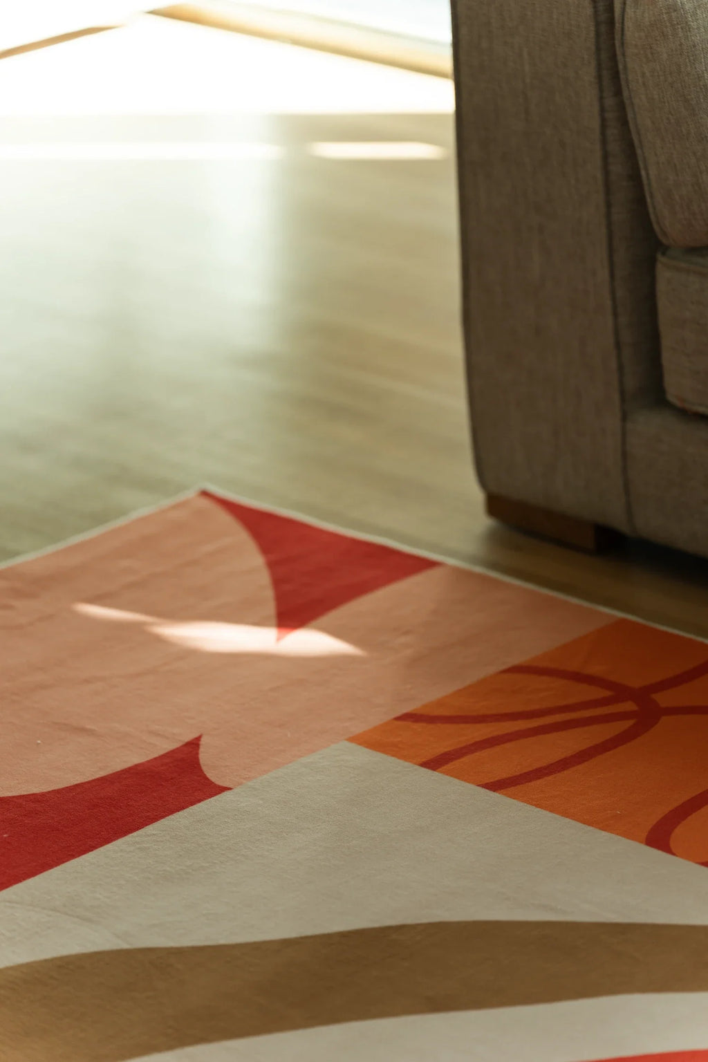 Close up beside the sofa with sunlight on the rug, highlighting a red star and orange hand drawn border lines
